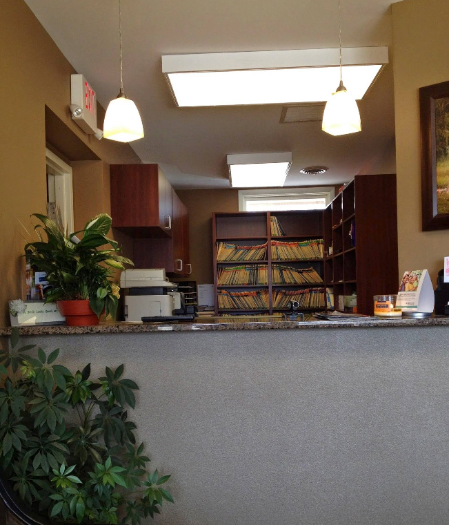 The image depicts an interior view of a reception area with a counter, shelves filled with books, and decorative elements such as plants and lamps.