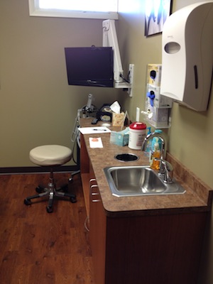 The image shows a medical office setting with a desk, sink, mirror, and various medical equipment.