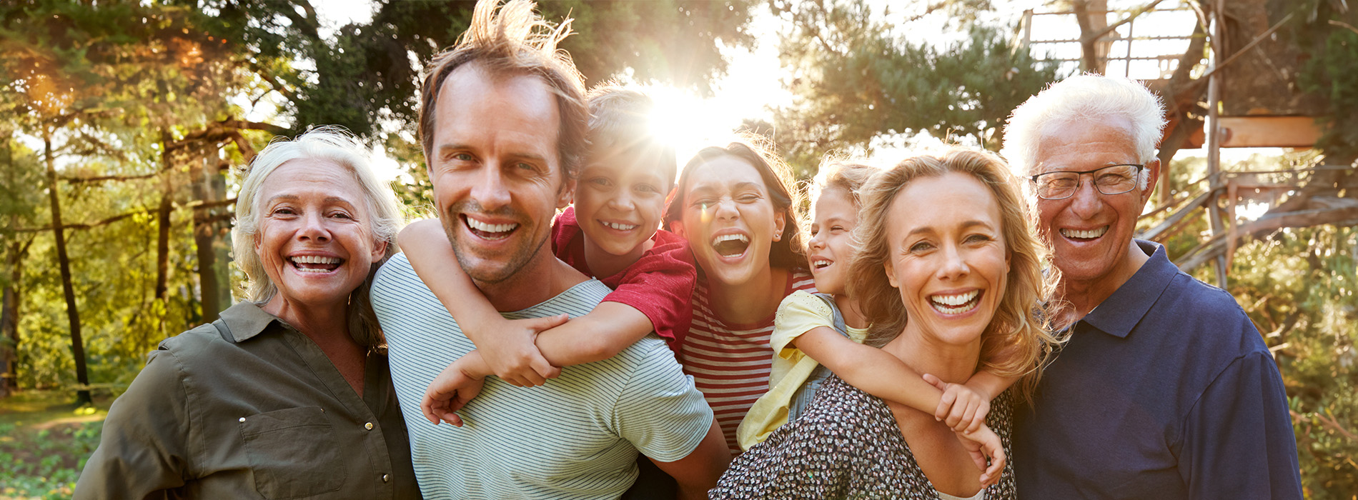 The image shows a family of four posing together outdoors during daylight with a warm, sunny atmosphere.