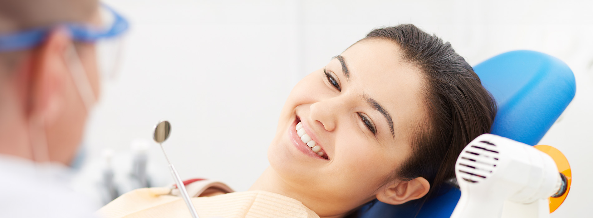 A young woman sitting in a dental chair with a smiling expression while undergoing dental treatment.