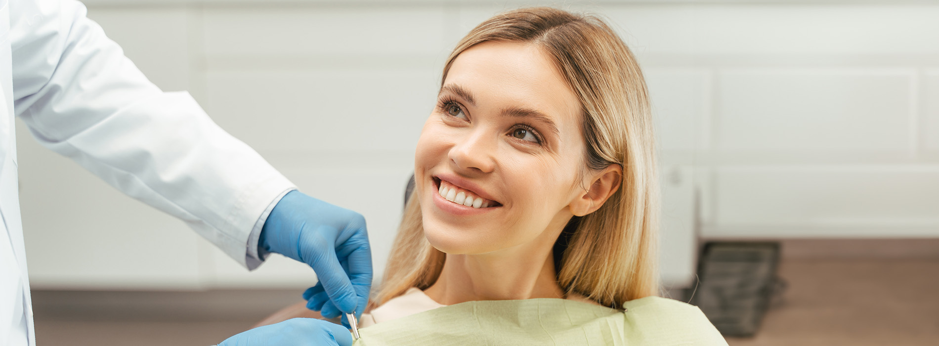 The image depicts a woman seated in a dental chair with a dental professional performing a procedure on her teeth.