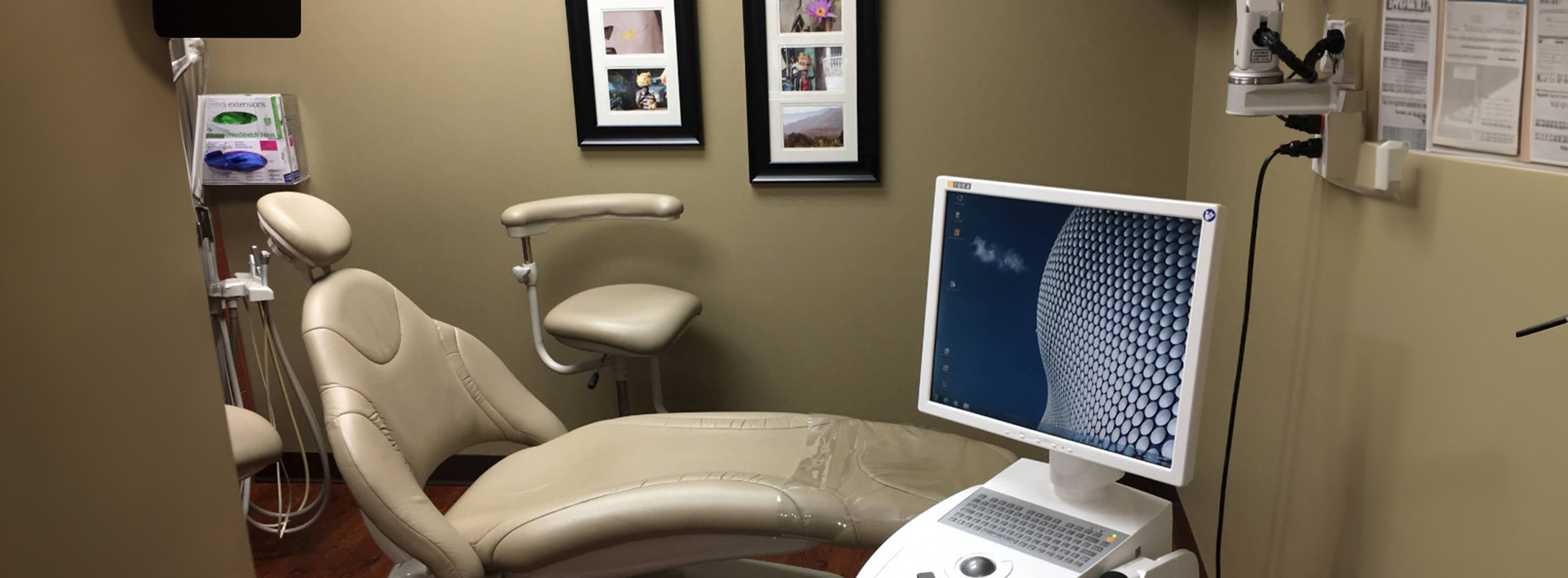 An interior view of a dental office with a chair, monitor, and equipment.